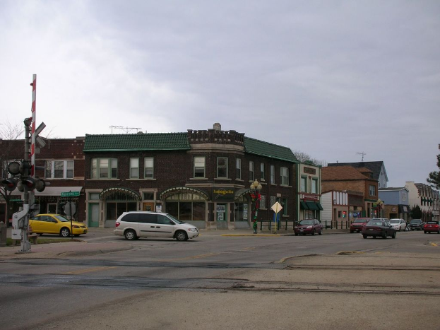 Mehrere Autos fahren auf einer Straße mit Gebäuden, Ampeln, einem Schild und einem Baum im Hintergrund.