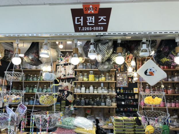 Ein unordentlicher Laden in Seoul, der verschiedene Gegenstände wie Körbe, Lichter, Flaschen und Spielzeuge auf Regalen ausstellt, mit einer Tafel öber der Tür, die ihn als einen der besten koreanischen Läden kennzeichnet.