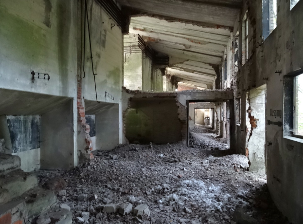 Altes Geb├Ąude mit erheblichen strukturellen Sch├Ąden, zerbrochene Fenster, verstreute Trümmmer, freiliegende Rohre und Schutt, die Verfall anzeigen.