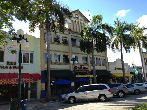 Einige Gebäude und Bäume mit mehreren Laternen und geparkten Autos auf der Seite.