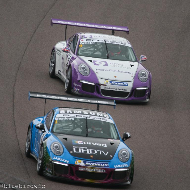 Zwei Autos auf einer Straße außerhalb einer Stadt mit Text in der unteren linken Ecke.