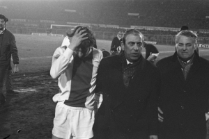 Eine Gruppe von bedrängten Männern in Schwarz-Weiß-Kleidung steht zusammen auf einem Fußballfeld, im Hintergrund ein Stadion.