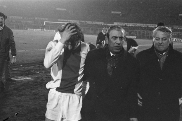 Eine Gruppe von bedrängten Männern in Schwarz-Weiß-Kleidung steht zusammen auf einem Fußballfeld, im Hintergrund ein Stadion.