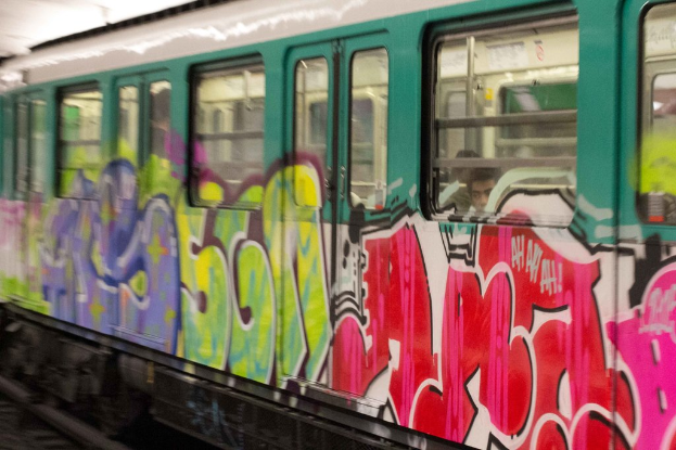 Ein Zug auf den Bahngleisen mit zwei Personen darin und Graffiti an seiner Außenseite.