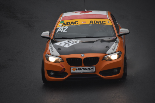 Oranges BMW-Rennfahrzeug mit sportlichem Text und Zahlen auf der Rennstrecke.