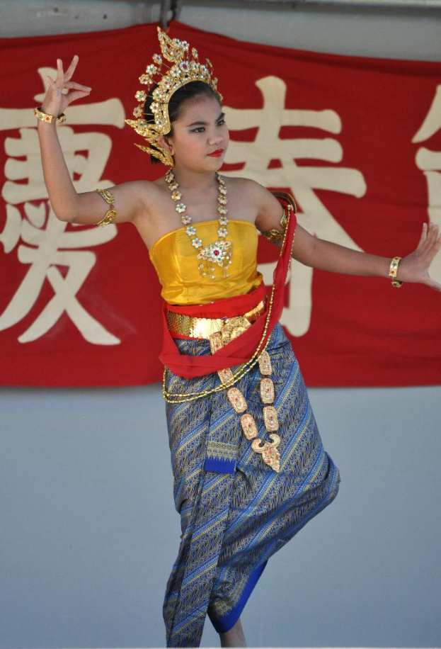 Ein Mädchen tanzt in einem kulturellen Kleid und Schmuck, mit einem Banner mit Text dahinter.