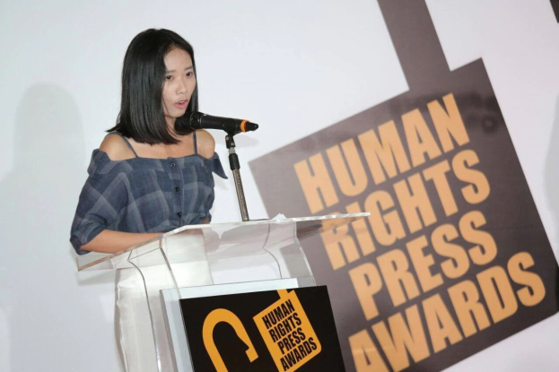 Frau in schwarzem Kleid und Dutt, die vor einem Mikrofon an einem Rednerpult steht und vor einem Banner mit der Aufschrift 'Human Rights Press Awards' spricht.
