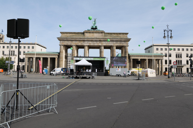 Das Brandenburgertor in Berlin, Deutschland, mit seinen ikonischen Säulen und Statuen, umgeben von Gebäuden, Laternenmasten, Verkehrssignalen, Zelten, Fahrzeugen, Menschen, Fahrrädern und grünen Luftballons am Himmel während des Berlin-Marathons.
