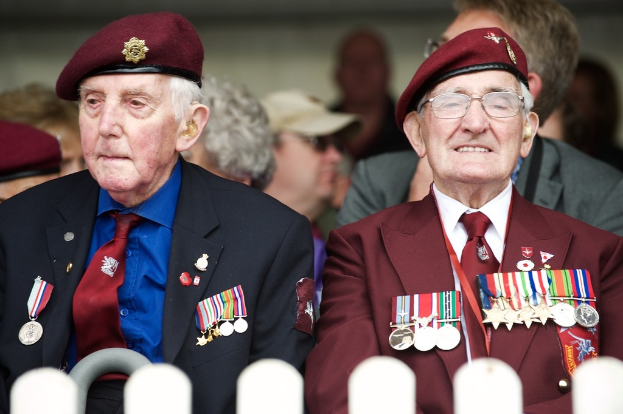 Zwei Personen in förmlicher Kleidung und braunen Mützen sitzen mit Medaillen geschmückt vor einem unscharfen Hintergrund.