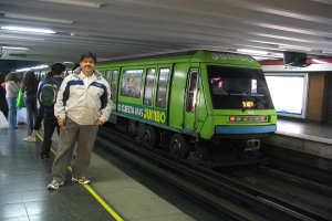 Ein Zug auf Schienen mit Menschen zu links und einem Dach oben im Bild.
