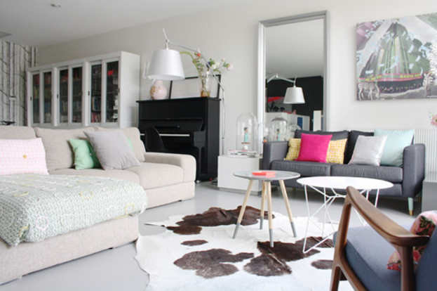 Ein Wohnzimmer mit zwei Sofas, zwei Tischen, einer Lampe, einem Kissen, einem Spiegel, einem Musikinstrument, einer Vitrine und einer Wand im Hintergrund.