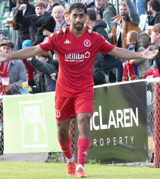Ein Fußballspieler in roter Uniform rennt mit ausgebreiteten Armen auf einem Feld, mit einer Menge und einem Banner mit der Aufschrift "Middlesbrough FC vs. Swansea City - Sky Bet Championship" im Hintergrund.