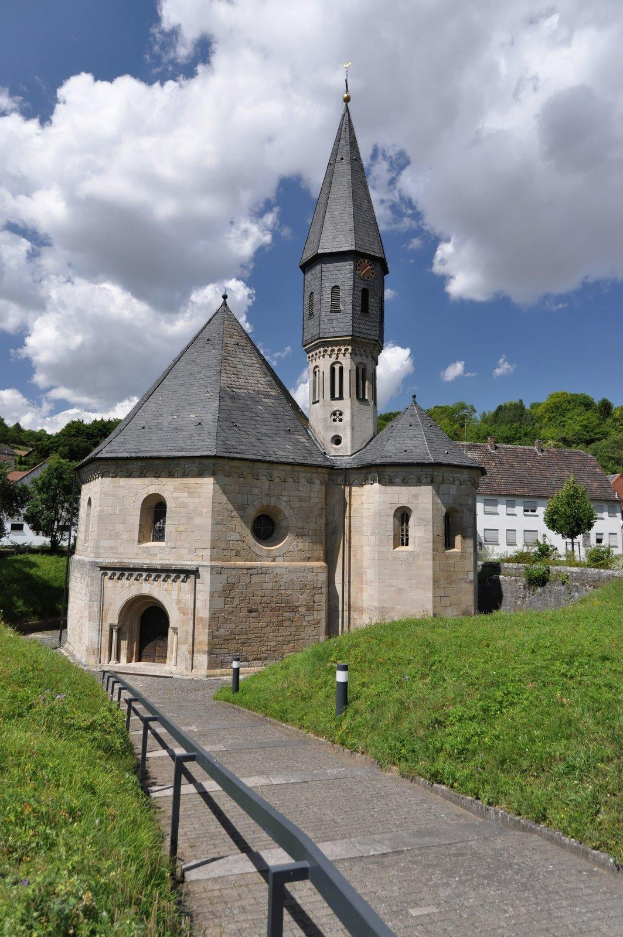 Alte steinerne Kirche mit einem zentralen Glockenturm und einem Kirchturm, umgeben von einem grasbewachsenen Feld, umgeben von Gebäuden, Bäumen und einem bewölkten Himmel in Lauterbrunnen, Deutschland.