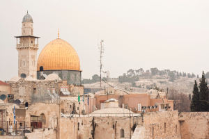 Mehrere Ziegelgebäude mit Satellitenschüsseln und Klimaanlagen vor einem Hintergrund aus Bäumen und Himmel