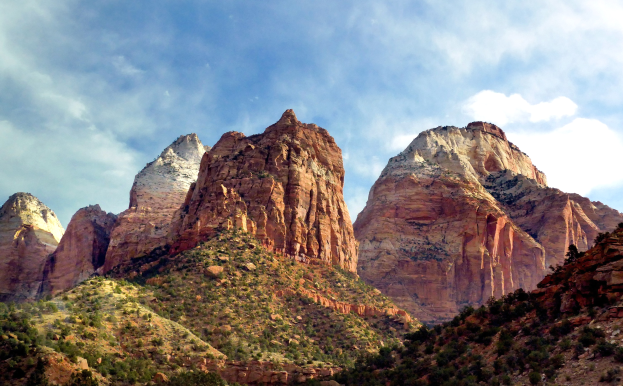 Towering mountains, lush trees, and rocky terrain of Zion National Park in Utah under a sky filled with white clouds.