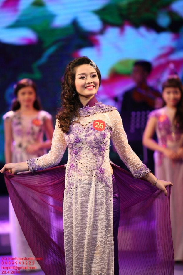 Eine Frau in einem cremefarbenen und lila Kleid mit einem Anstecker darauf, mit einem unscharfen Hintergrund.