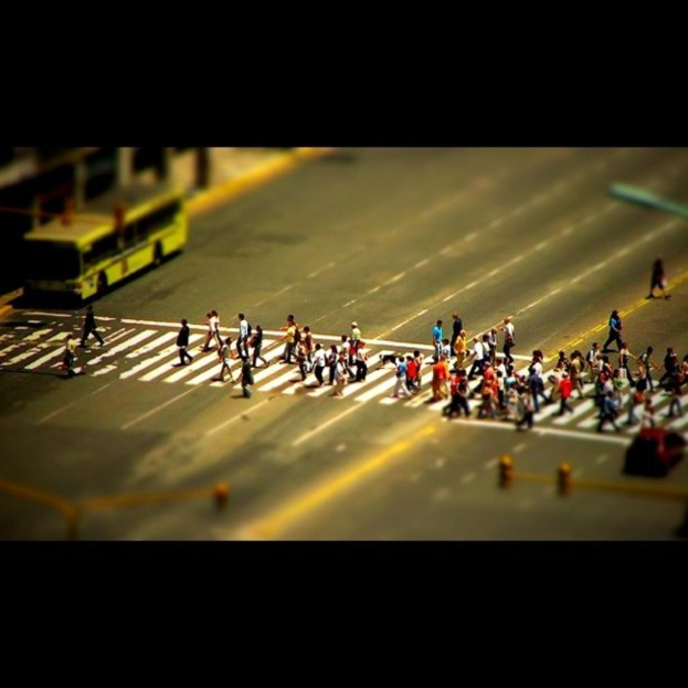 Eine Straße mit Menschen, die zu Fuß gehen, ein Bus, Ampeln und ein Auto auf der rechten Seite.