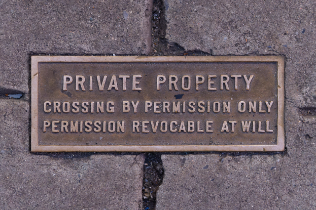 Ein rechteckiges Schild auf dem Gehweg mit einem wei├čem Hintergrund und fetter schwarzer Schrift, die den Text "Privateigentum ├ťberqueren nur mit Erlaubnis" angezeigt.