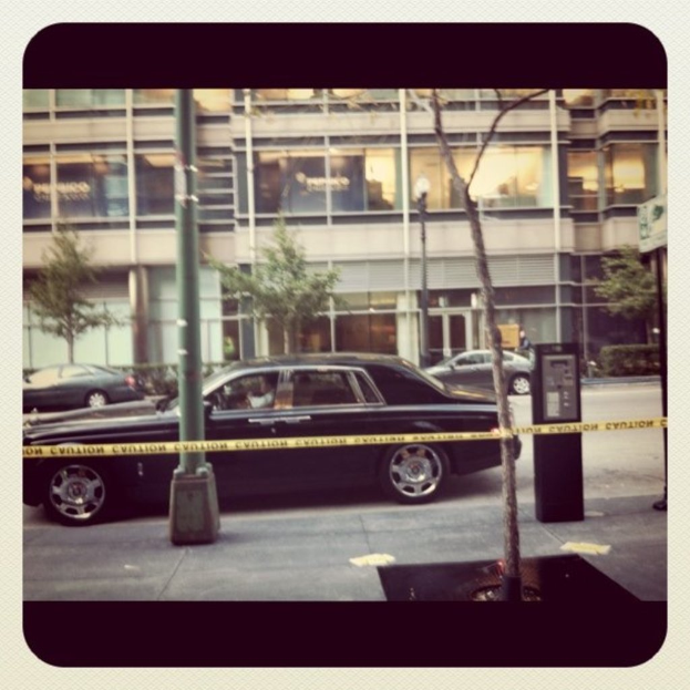 Ein Auto ist in der Mitte eines Bildes mit Pfählen und Bäumen, einem Gebäude, Fahrzeugen und Pflanzen im Hintergrund und einem Weg am Boden geparkt.