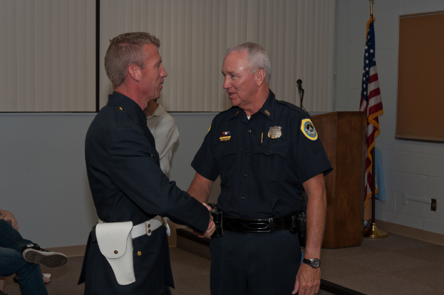 Zwei männer in uniformen schütteln sich die hände vorne, mit zwei personen und einer wand im hintergrund und einem podium, mikrofon und flagge auf der rechten seite.