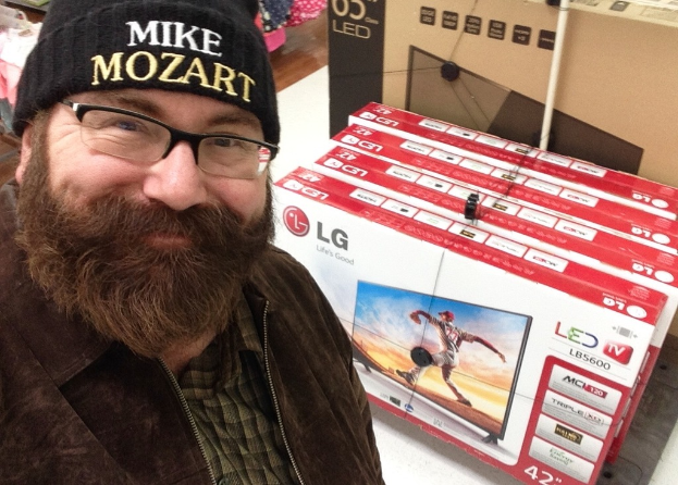 Ein Person lacht vor Fernsehgeräten in Kartons und anderen Gegenständen.