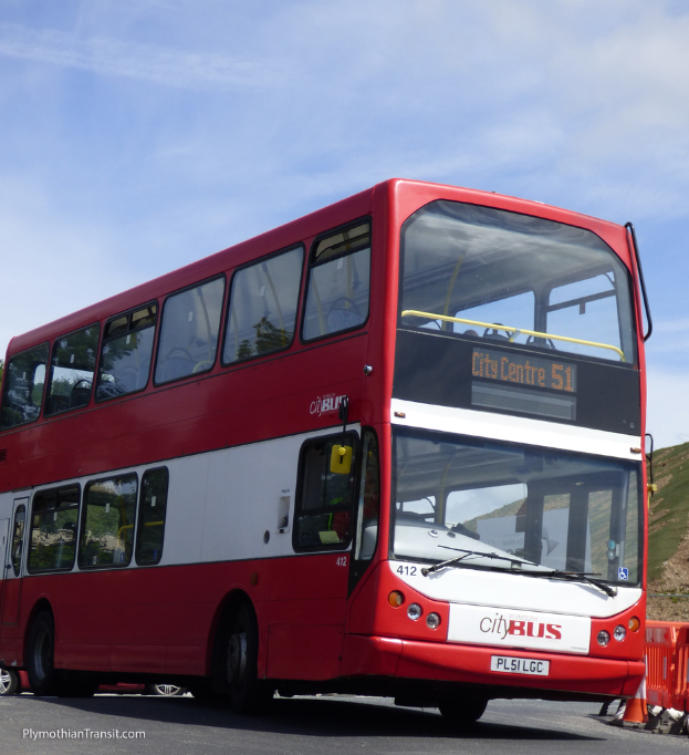 Ein roter Doppeldeckerbus mit der Aufschrift 'Stadtbus' f√§hrt auf einer Stra√e mit einer Verkehrskegel und einem Hügel im Hintergrund.