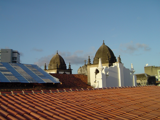 Stadtansicht mit Gebäuden im Vordergrund, einem blauen Himmel im Hintergrund und Solarpanelen auf dem Dach eines Gebäudes.