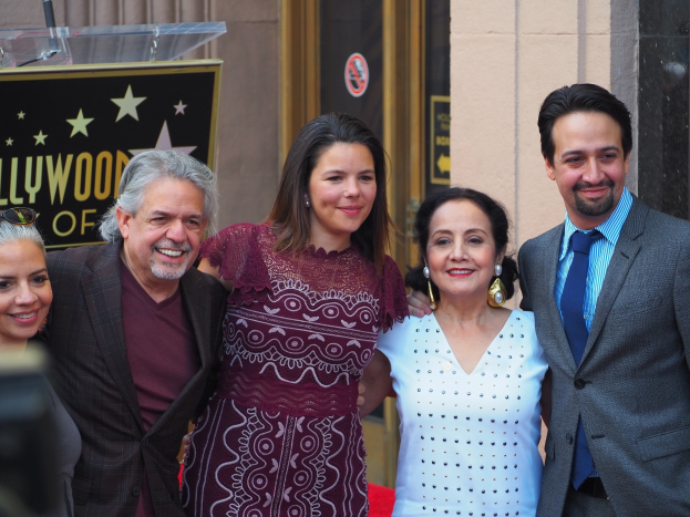 Gruppe von Menschen, die auf dem roten Teppich der Zeremonie des Hollywood Walk of Fame posieren, mit einer Tafel, einem Glaspodest und einer Wand im Hintergrund.
