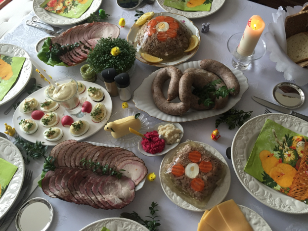 Ein für ein traditionelles deutsches Osteressen gedeckter Tisch mit verschiedenen Gerichten, Besteck, Gläsern, Kerzen und umliegenden Stühlen.
