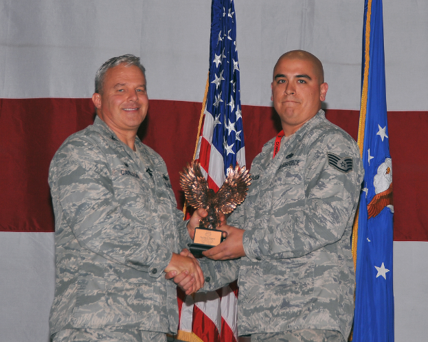 Zwei Personen mit einer Auszeichnung, mit Flaggen und einem Vorhang im Hintergrund.