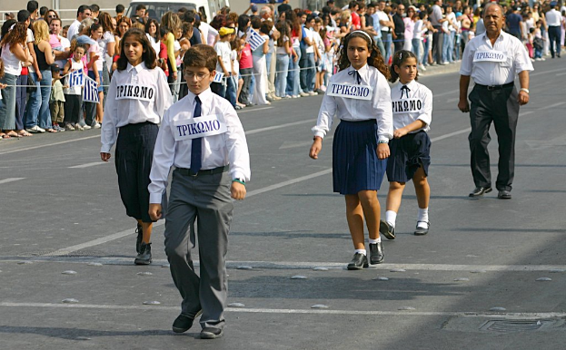 Eine Frau in schwarzer Oberbekleidung sitzt auf einem Stuhl und schaut geradeaus, neben ihr ein Mann in einem blauen Hemd; im Hintergrund sind ein Award-Trophy und ein gelbes Plakat zu sehen.