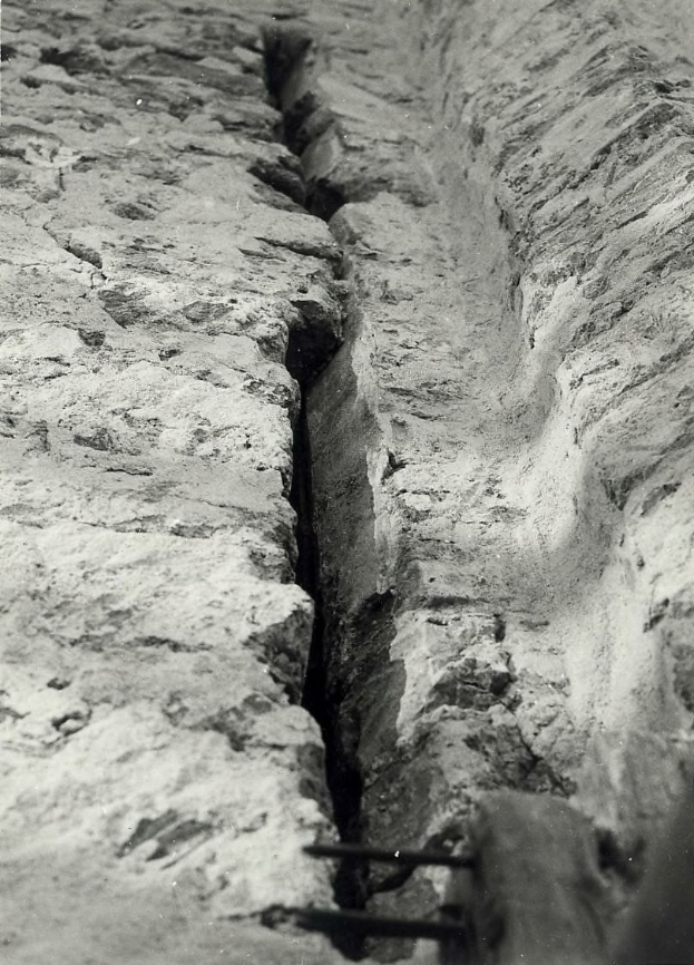 Schwarzes und weiße Foto eines großen Risses im Boden, wahrscheinlich ein Entwässerungskanal, mit einem sichtbaren Wasserzeichen auf der linken Seite.