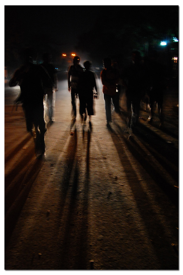 Mehrere Personen auf einer Straße mit einem Licht hinter ihnen und zusätzlichen Lichtern im Hintergrund.