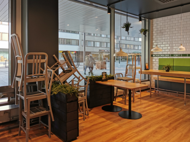 Ein Restaurant mit hölzernen Tischen und Stühlen drinnen, durch ein großes Fenster betrachtet, das Menschen auf einer Berliner Straße mit Gebäuden, Pfählen und Himmel zeigt.