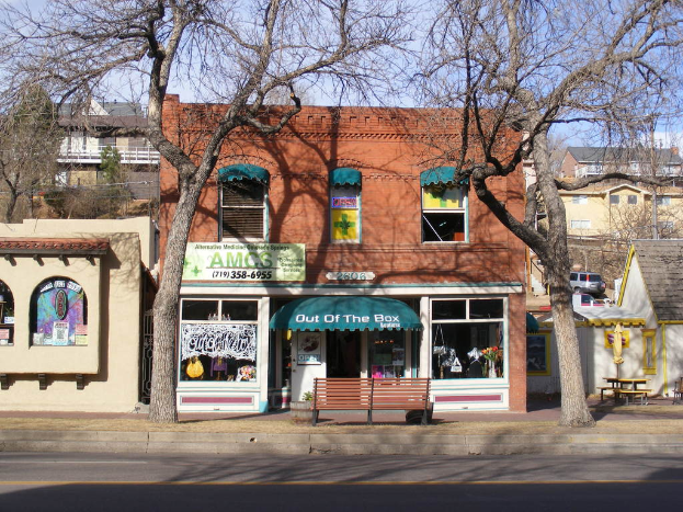 Eine Stra√üe mit Geb√§uden, B√§nken, B√§umen, einem Fahrzeug und dem Himmel im Hintergrund.