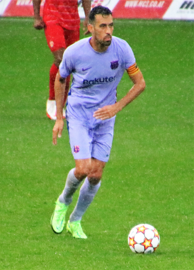 Ein Fußballer in Sportbekleidung und -schuhen ist im Einsatz auf dem Feld, mit einer Texttafel im Hintergrund.