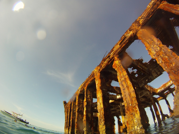Ein Schiff fährt auf dem Wasser in der unteren linken Ecke des Bildes, mit einem hölzernen Dock auf der rechten Seite.