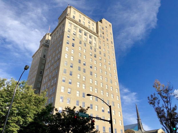 Historisches Marshall-Hotel-Gebäude mit zahlreichen Fenstern, umgeben von Straßeninfrastruktur einschließlich Pfählen, Lampen, Signalen und Namensschildern, mit Bäumen und einem bewölkten Himmel im Hintergrund.