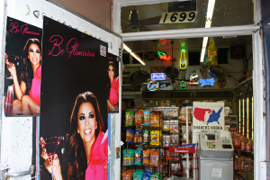 Eine Innenaufnahme mit einer Tür mit Postern einer Frau auf der linken Seite, verschiedenen Ladenartikeln in der Mitte, einem Geldautomaten und einer Texttafel auf der rechten Seite und einer Nummerntafel oben.