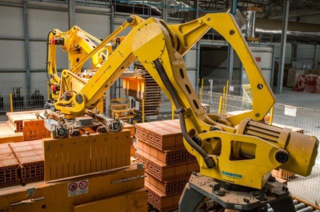 Ein großes Lagerhaus voller numerous boxes, Kräne und verschiedene industrielle Ausrüstung, mit einem Zaun und Polen im Vordergrund und einer Wand im Hintergrund.