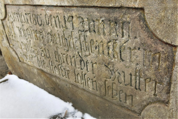 Ein steinernes Schild an einem Gebäude, bedeckt von Schnee, mit Text, der wahrscheinlich Holocaust-Opfer gedenkt.