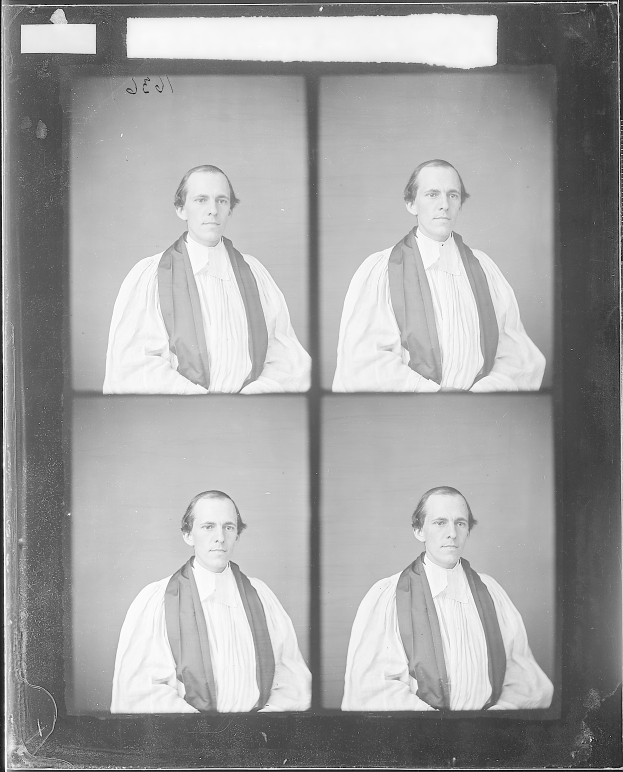 Ein Schwarz-Weiß-Foto eines Mannes in einem weißen Hemd und einem schwarzen Cape, mit ernstem Gesichtsausdruck, ordentlich frisiertem Haar und gefalteten Händen, der konzentriert in die Ferne blickt.