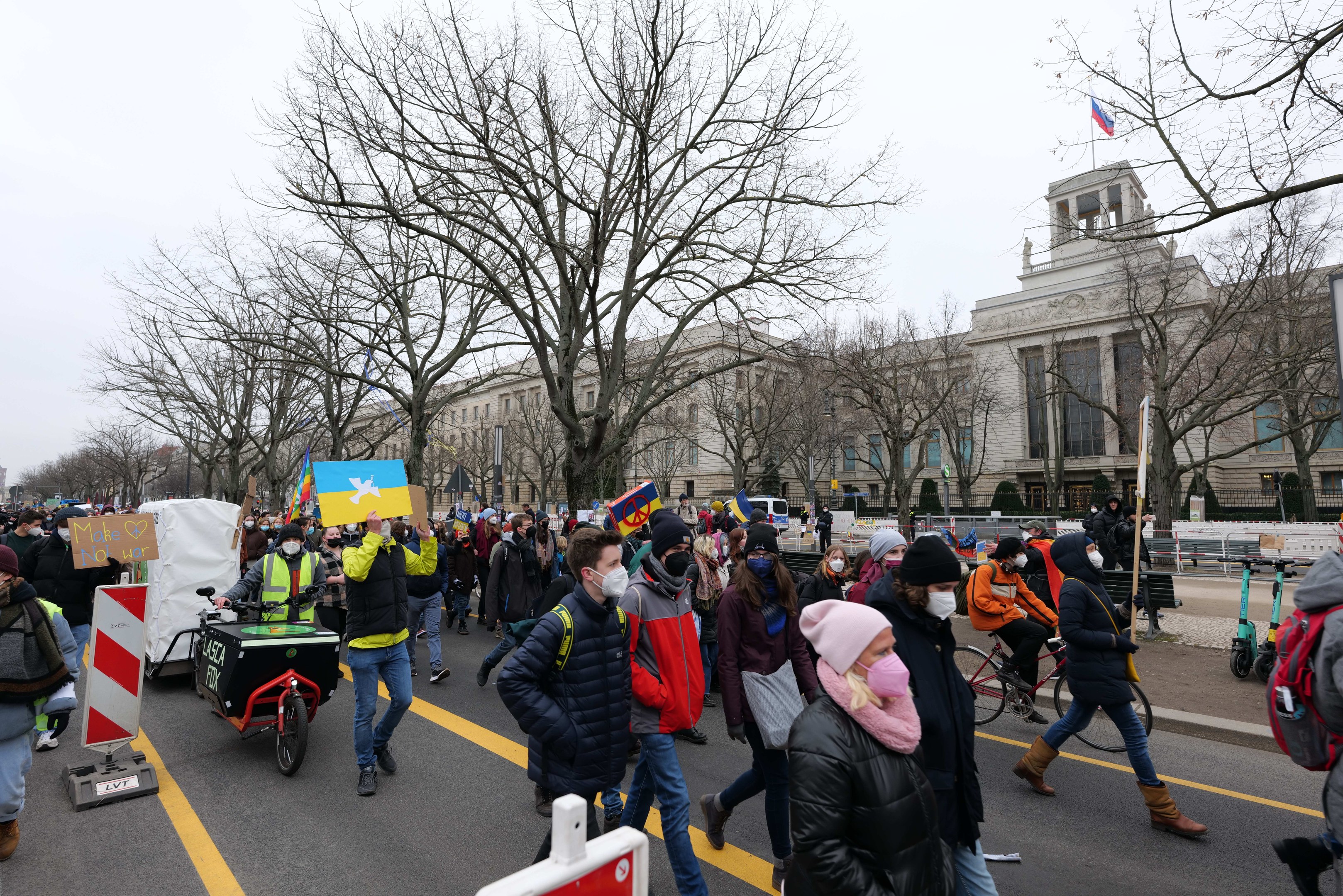 Eine große Gruppe von Menschen marschiert bei einer Protestaktion in Washington, D.C. durch die Straßen, hält Schilder und Banner hoch und fährt mit Fahrrädern, unter einem klaren blauen Himmel.