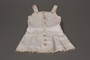 Ein weißes Kleid mit klassischem Schnitt, rundem Halsausschnitt, kurzen Ärmeln und einem weiten Rock, mit symmetrischen Knöpfen und einem dezenten Glanz liegt auf einer grauen Oberfläche.