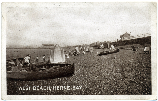 Schwarzes und weißes Foto von Menschen am Weststrand in Herne Bay mit Booten im Vordergrund, H├Ąusern und einem Zaun im Hintergrund und Text unten.