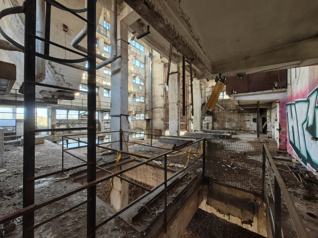 Verlassenes Gebäudeinnere mit Graffiti-beschmierten Wänden, bröckelnden Strukturen, gebrochenen Fenstern, Geländern, Polen, Rohren und Pipelines; sichtbares Wasserzeichen unten.