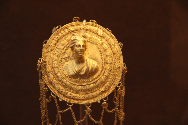 Goldene Medaille mit einer Frauengestalt auf dunklem Hintergrund, mit feiner Verzierung und königlichem Aussehen.