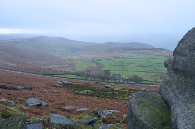 Eine Landschaft mit großen Felsen und Steinen im Vordergrund und Feldern und Bergen im Hintergrund.
