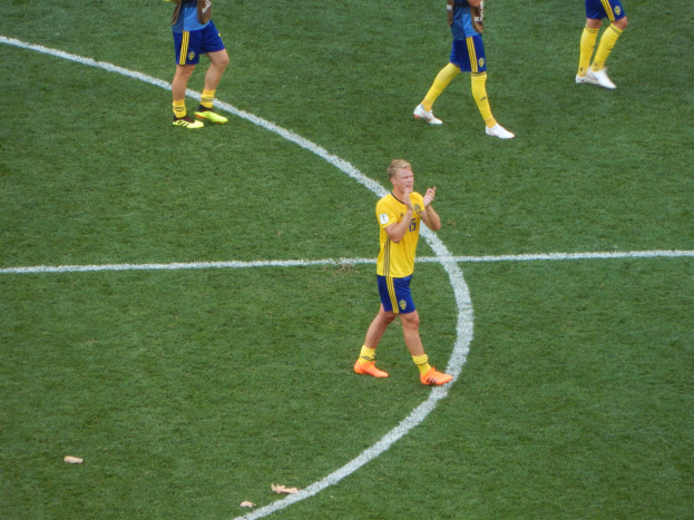 Eine Gruppe von Männern in Fussballtrikots und -schuhen steht auf einem Fussballfeld, wobei eine Person in der Mitte klatscht.
