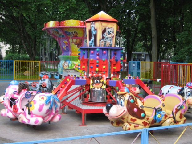 Buntes Karussell mit Geländer, umgeben von Bäumen, in einem Vergnügungspark mit zusätzlichen Kinderfahrten.